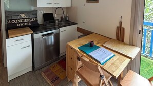 Une cuisine de taille réduite avec des meubles blancs, un lave-vaisselle en acier inoxydable et une table à manger en bois, accompagnée de chaises.