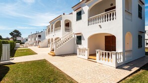A white building with multiple balconies, a staircase, and a paved courtyard.