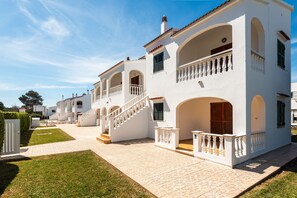 A white building with multiple balconies, a staircase, and a paved courtyard.