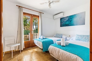 A room with two beds, a chair, a balcony door, and an air conditioning unit.