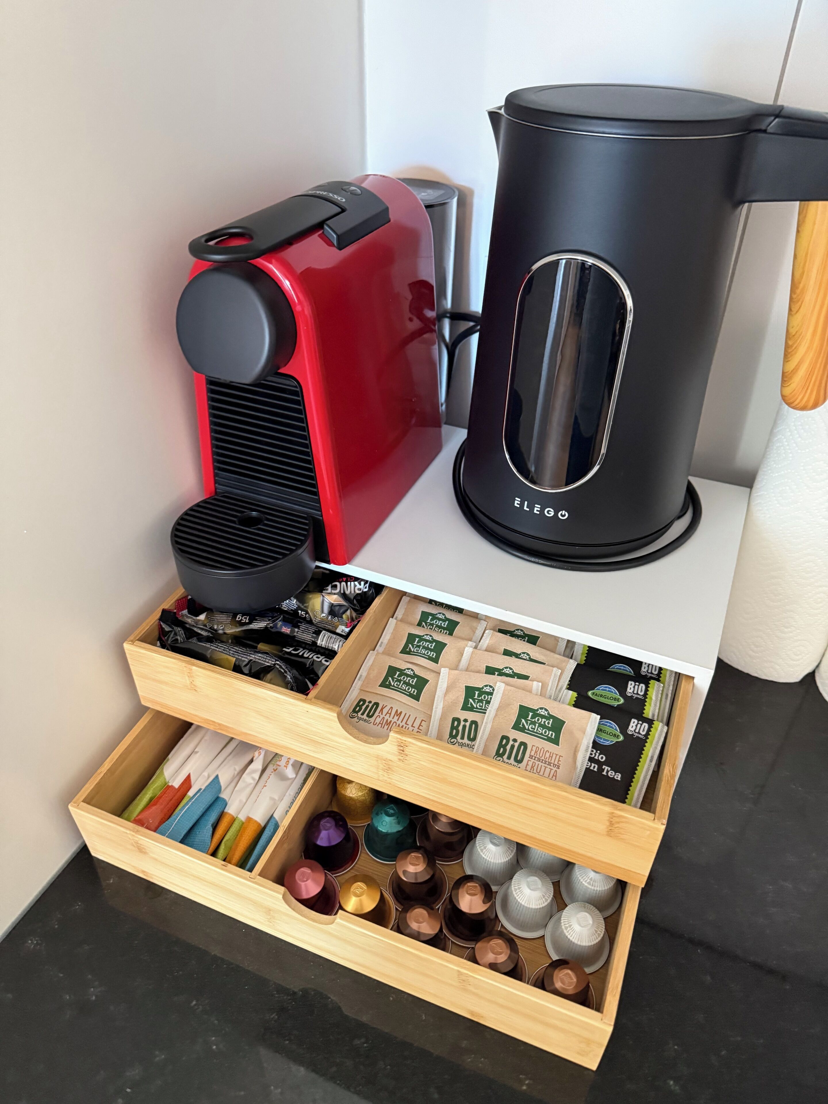 Una cafetera, un hervidor y un cajón con bolsitas de té y cápsulas de café.