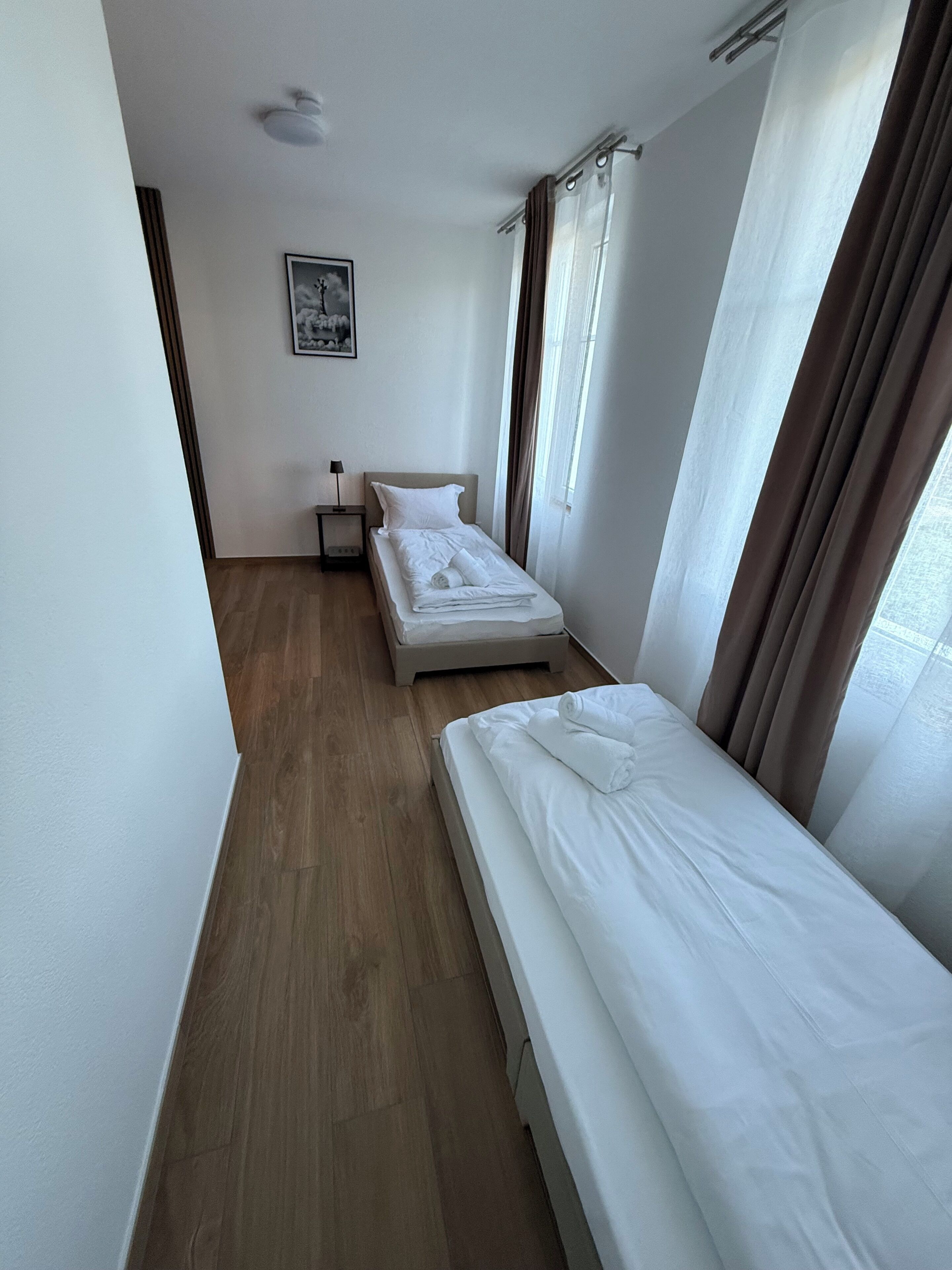 A hotel room with two beds, a nightstand, a lamp, and a framed picture on the wall.