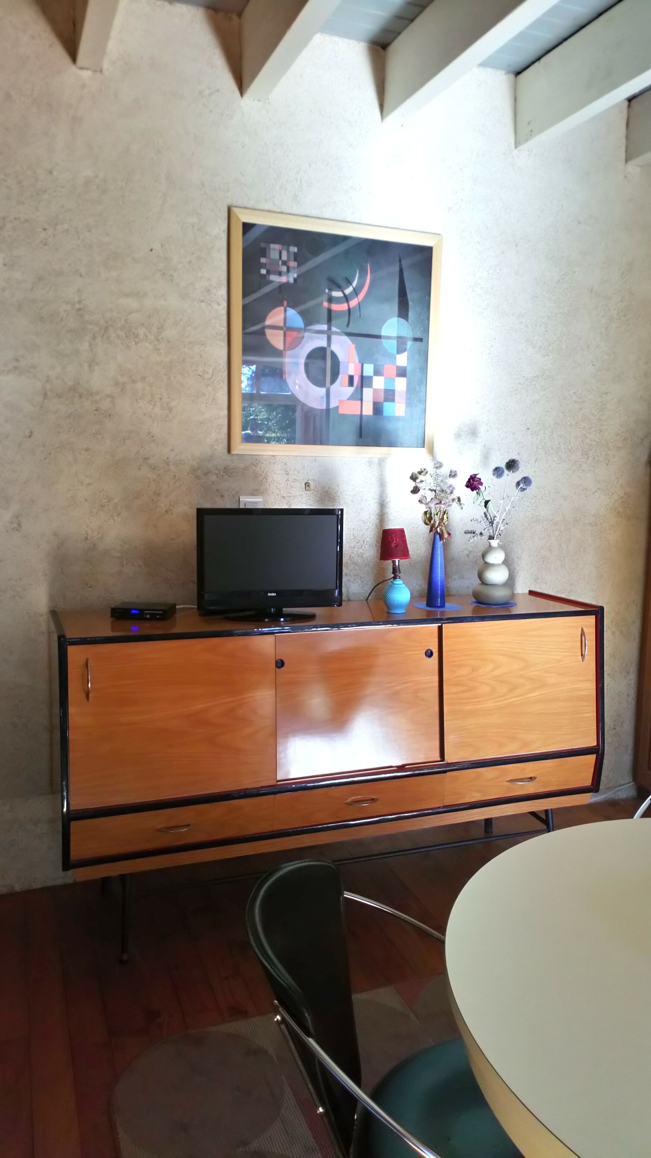 Ein Zimmer mit einem Holzschrank, einem Fernseher, einer Blumenvase und einem Bild an der Wand.