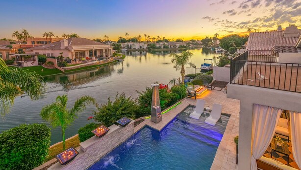 A swimming pool with a waterfall feature, surrounded by palm trees and a view of a lake at sunset. - Waterfront,FREE Heated Pool, Spa & therapy Jets! Boat &Kayak! Indoor slides! (Chandler)