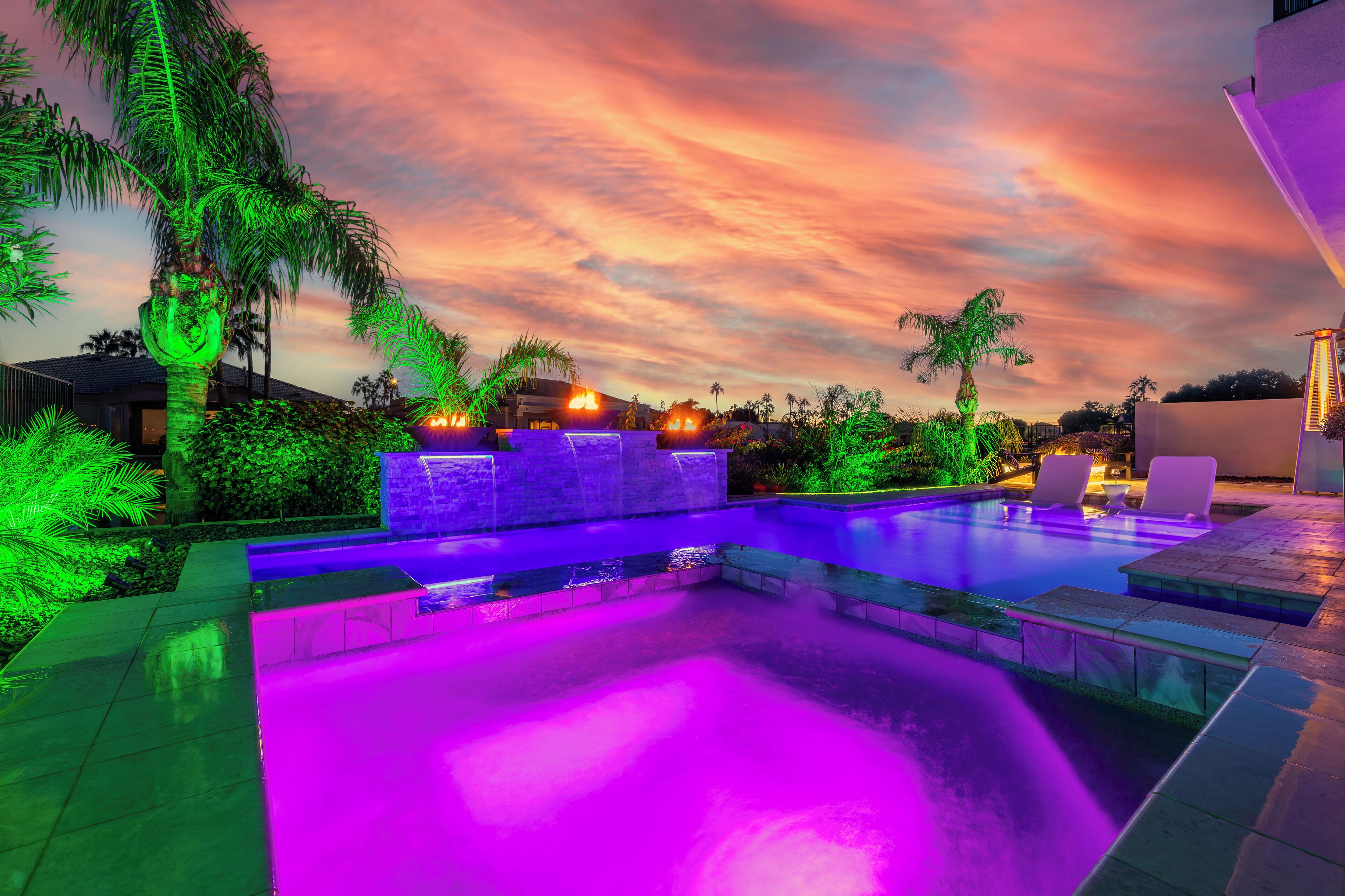 Ein Pool mit Wasserfall, umgeben von Palmen und einem Sonnenuntergangshimmel.