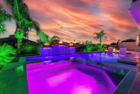 A swimming pool with a waterfall feature, surrounded by palm trees and a sunset sky. - Waterfront,FREE Heated Pool, Spa & therapy Jets! Boat &Kayak! Indoor slides! (Chandler)