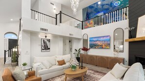A spacious living room with a high ceiling, a staircase, and a cityscape painting. - Waterfront,FREE Heated Pool, Spa & therapy Jets! Boat &Kayak! Indoor slides! (Chandler)