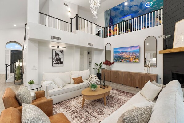 A spacious living room with a high ceiling, a staircase, and a cityscape painting. - Waterfront,FREE Heated Pool, Spa & therapy Jets! Boat &Kayak! Indoor slides! (Chandler)