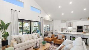 A modern living room with a sofa, armchairs, and a coffee table. There is a kitchen area with white cabinets and appliances. - Waterfront,FREE Heated Pool, Spa & therapy Jets! Boat &Kayak! Indoor slides! (Chandler)