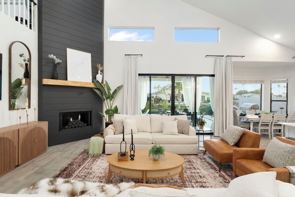 A modern living room with a fireplace, a sofa, a coffee table, and a view of the outdoors. - Waterfront,FREE Heated Pool, Spa & therapy Jets! Boat &Kayak! Indoor slides! (Chandler)