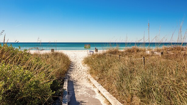 En stig som leder från stranden ner till havet, med en träpromenad och en informationsskylt.