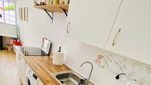 Une cuisine moderne dotée d’un plan de travail en bois, d’un évier en acier inoxydable, d’un lave-linge encastré et de meubles de rangement blancs.