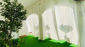 Une pièce avec une moquette verte, des murs blancs et un grand arbre dans un coin.