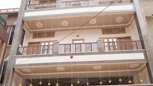 A multi-story building with a central entrance, decorative railings, and a sign indicating a business establishment. - Nidhipataye Homestay (Varansi)