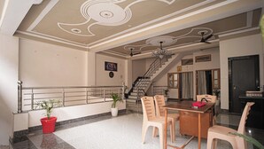 A spacious living area with a dining table, chairs, a staircase, and a kitchen area. - Nidhipataye Homestay (Varansi)