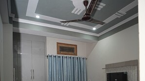 A bedroom with a bed, a ceiling fan, a TV mounted on the wall, and a wardrobe. - Nidhipataye Homestay (Varansi)