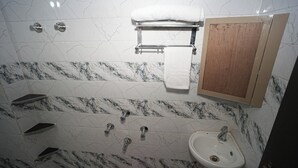 A bathroom with a marble-tiled wall, a white sink, a towel rack, and a wooden cabinet. - Nidhipataye Homestay (Varansi)