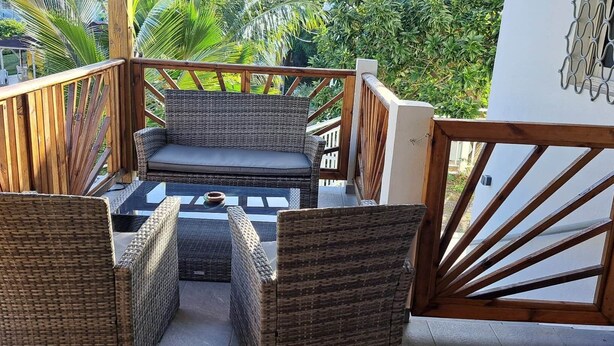 A balcony with wicker furniture, a glass table, and a view of the surrounding greenery. - Ti Zeinga the (Sainte-Anne)