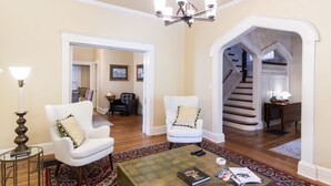 A spacious living room with a large coffee table, two white armchairs, a chandelier, and a staircase leading to another level. - Ultimate Getaway: Expansive Home with Hot Tub & Relaxation (Louisville)