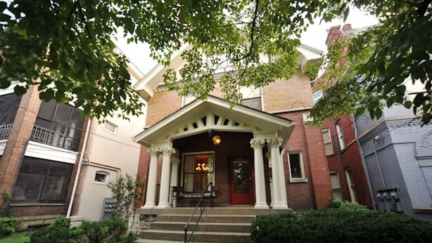 A two-story building with a central entrance featuring a porch with columns, a red door, and a small seating area with a table and chairs. - Ultimate Getaway: Expansive Home with Hot Tub & Relaxation (Louisville)