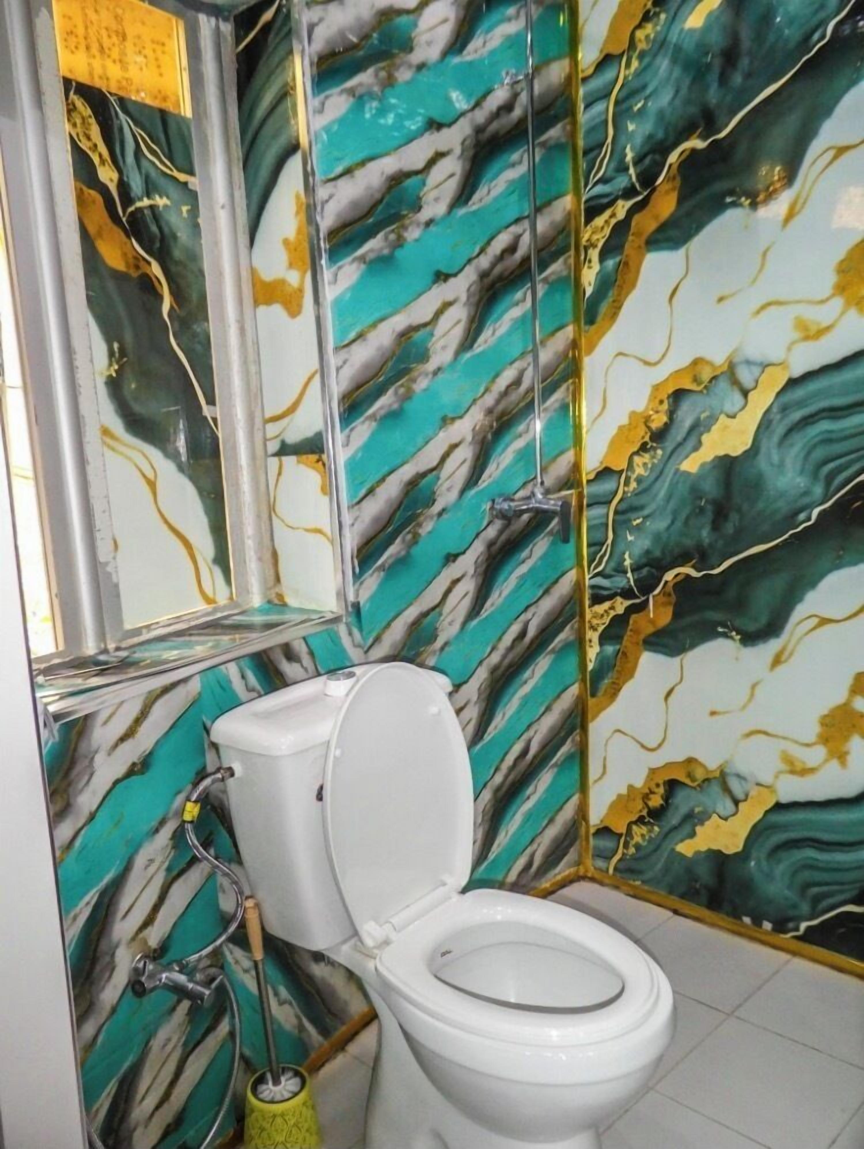 Un baño con pared de diseño de mármol, un inodoro blanco y un cepillo amarillo para limpieza.