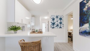 Ett modernt kök med vita skåp, en köksö och en matplats med stolar i rotting.