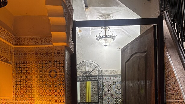 Una vista interna di una tradizionale stanza marocchina con pareti in piastrelle decorate, una porta in legno e un lampadario.