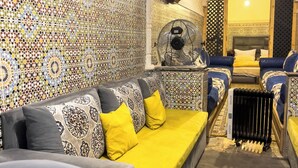 Una stanza con parete decorata, un divano con cuscini gialli, una ventola e un termosifone.