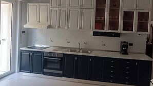 Une cuisine avec des meubles blancs, une cuisinière noire et une machine à café.