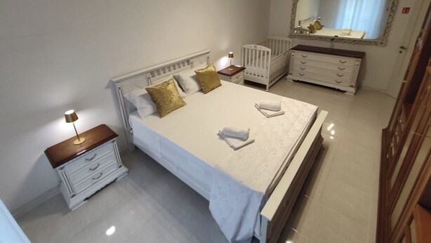 Une chambre à coucher comprenant un lit, une table de chevet, une commode, un berceau et un miroir.
