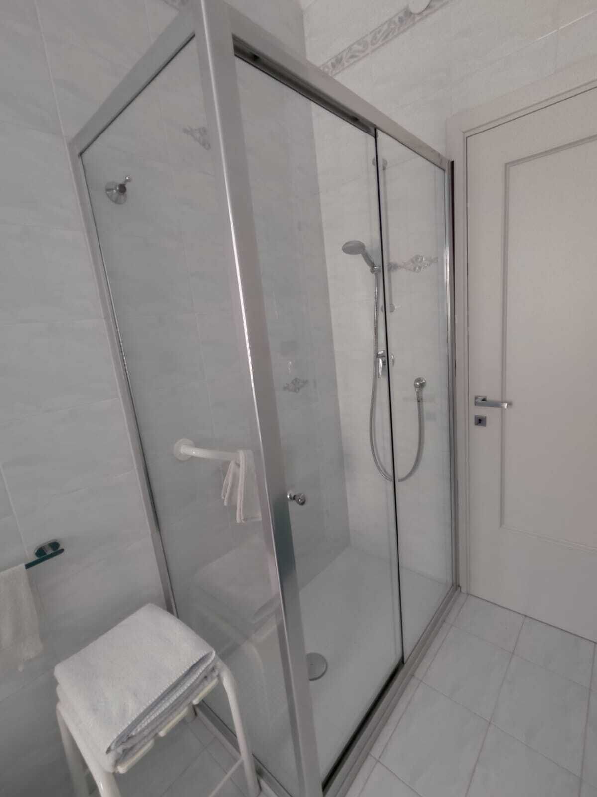 Een moderne badkamer met een douchecabine van glas, een witte deur en een kleine witte handdoek op een krukje.