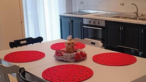 Un coin repas avec une table blanche, des sets de table rouges et des chaises noires.