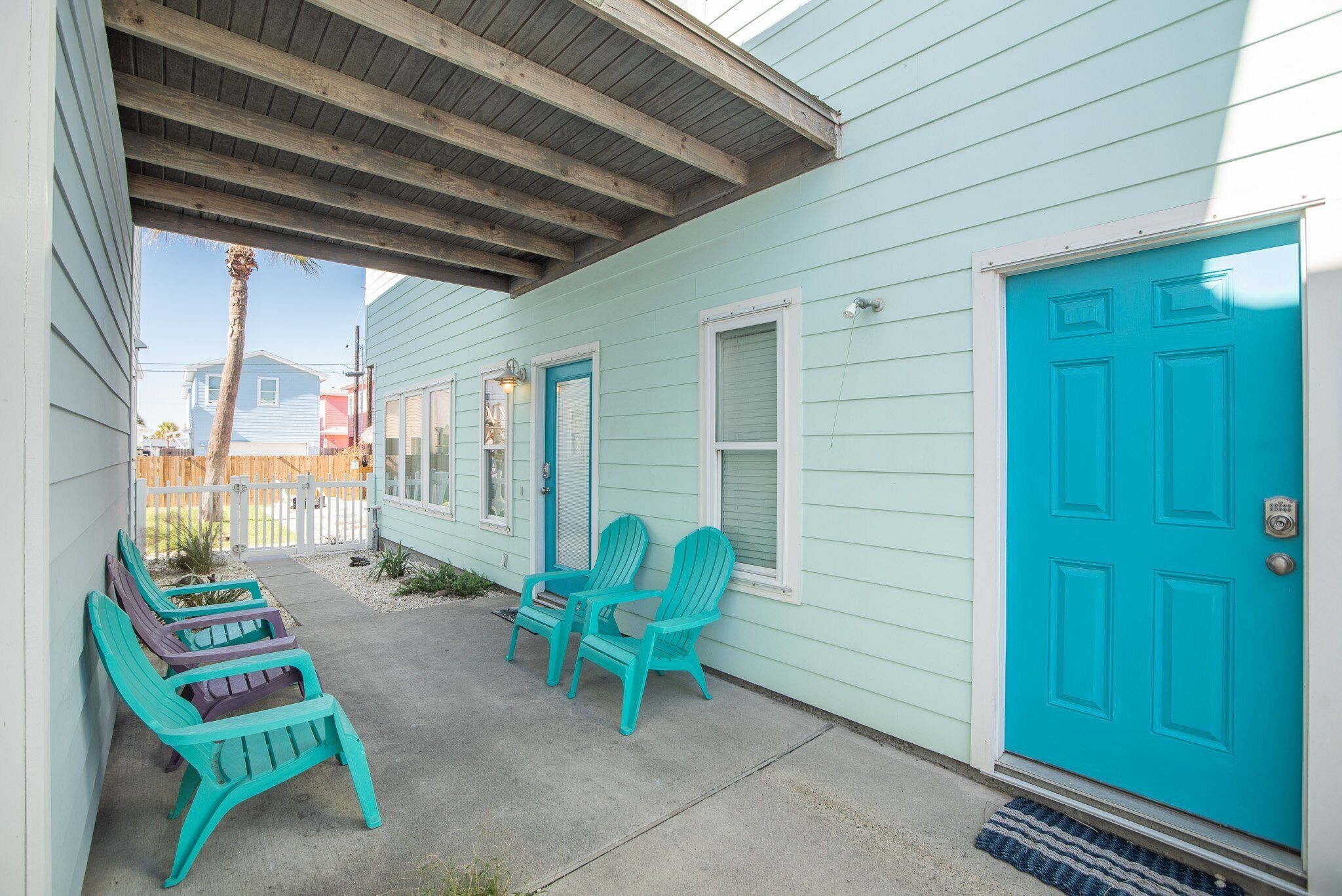 A covered porch with two Adirondack chairs and a blue door.
