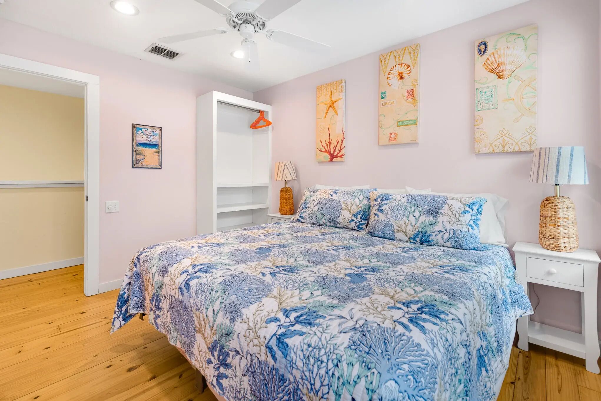A bedroom with a bed, a nightstand, a lamp, a hanging coat rack, and wall art.