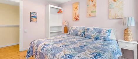 A bedroom with a bed, a nightstand, a lamp, a hanging coat rack, and wall art.