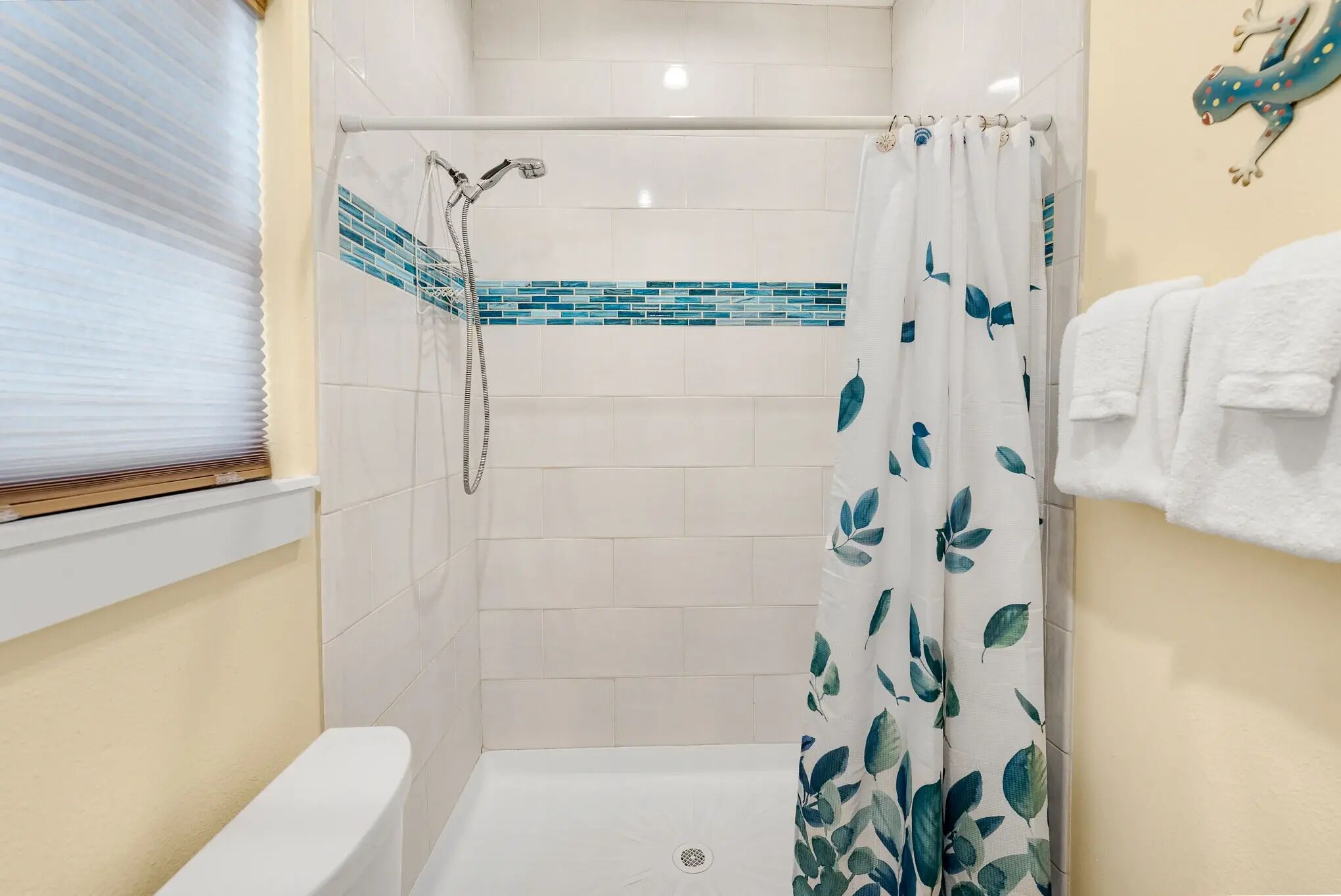 Ein Duschbereich mit einer weißen Badewanne, einer Duschbrause und einem Vorhang mit Blattmuster.