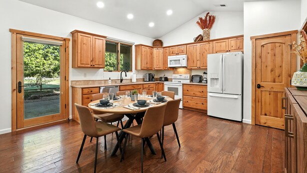 Una cucina moderna con mobili in legno, un tavolo da pranzo con sedie, una ventola a soffitto e vista panoramica attraverso una porta vetrata.