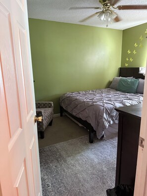 Een slaapkamer met een bed, een stoel, een plafondventilator en een deur.