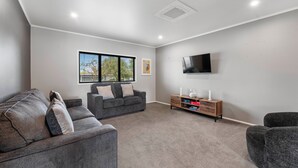 Ein modernes Wohnzimmer mit einem grauen Sofa, einem kleineren grauen Sessel, einem Holznachttisch und einem an der Wand befestigten Flachbildfernseher.