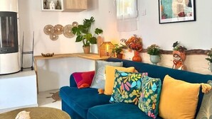 Uma sala de estar moderna com um sofá azul, uma mesa de centro e uma área de cozinha com uma geladeira branca e armários de madeira.
