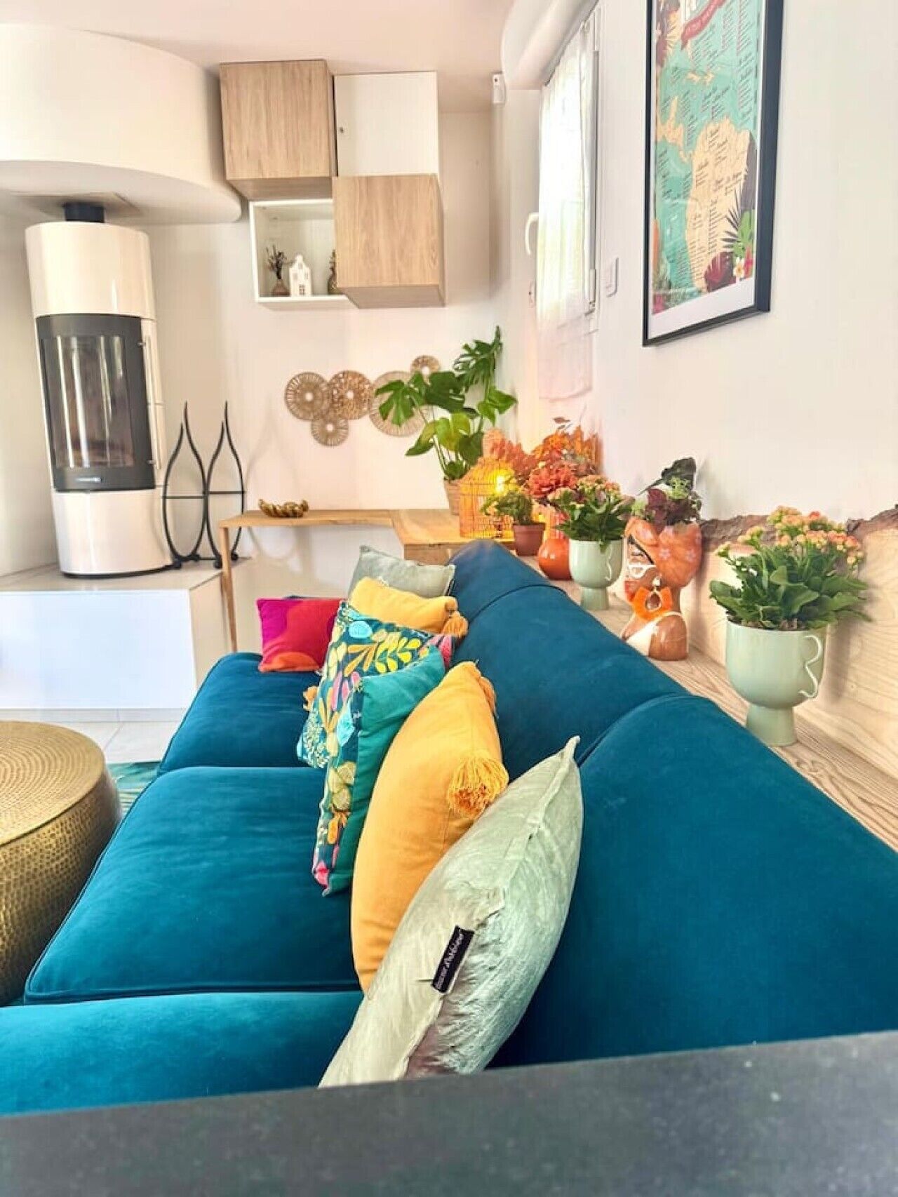 Een woonkamer met een blauwgroene bank, decoratieve kussens, een houten kast, een kaart aan de muur en een kleine tafel met planten.