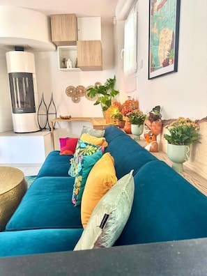 A living room with a teal sofa, decorative pillows, a wooden cabinet, a map on the wall, and a small table with plants.