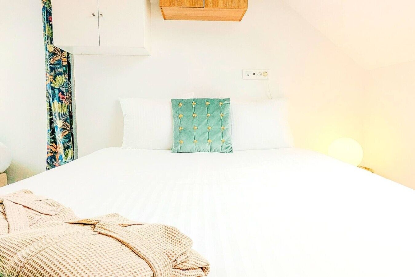 Een slaapkamer met een bed, nachtkastje, lamp en raam.