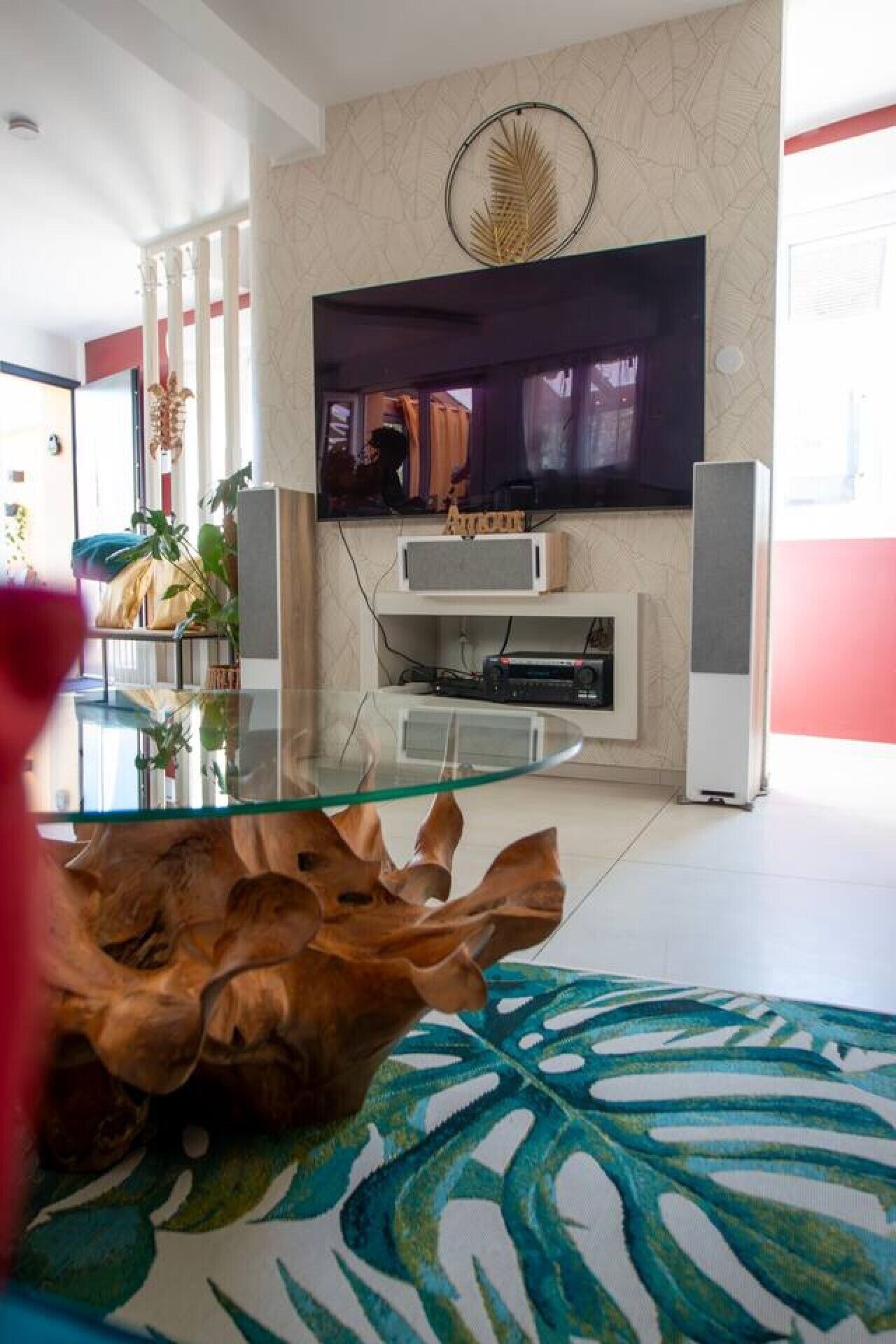 Un soggiorno moderno con un tavolino in vetro, una TV a schermo piatto montata a parete e un tappeto decorato con un motivo a foglia.