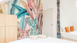 Quarto de hotel com uma cama grande, um guarda-roupa, uma porta e uma cortina com estampa de folhagem tropical.