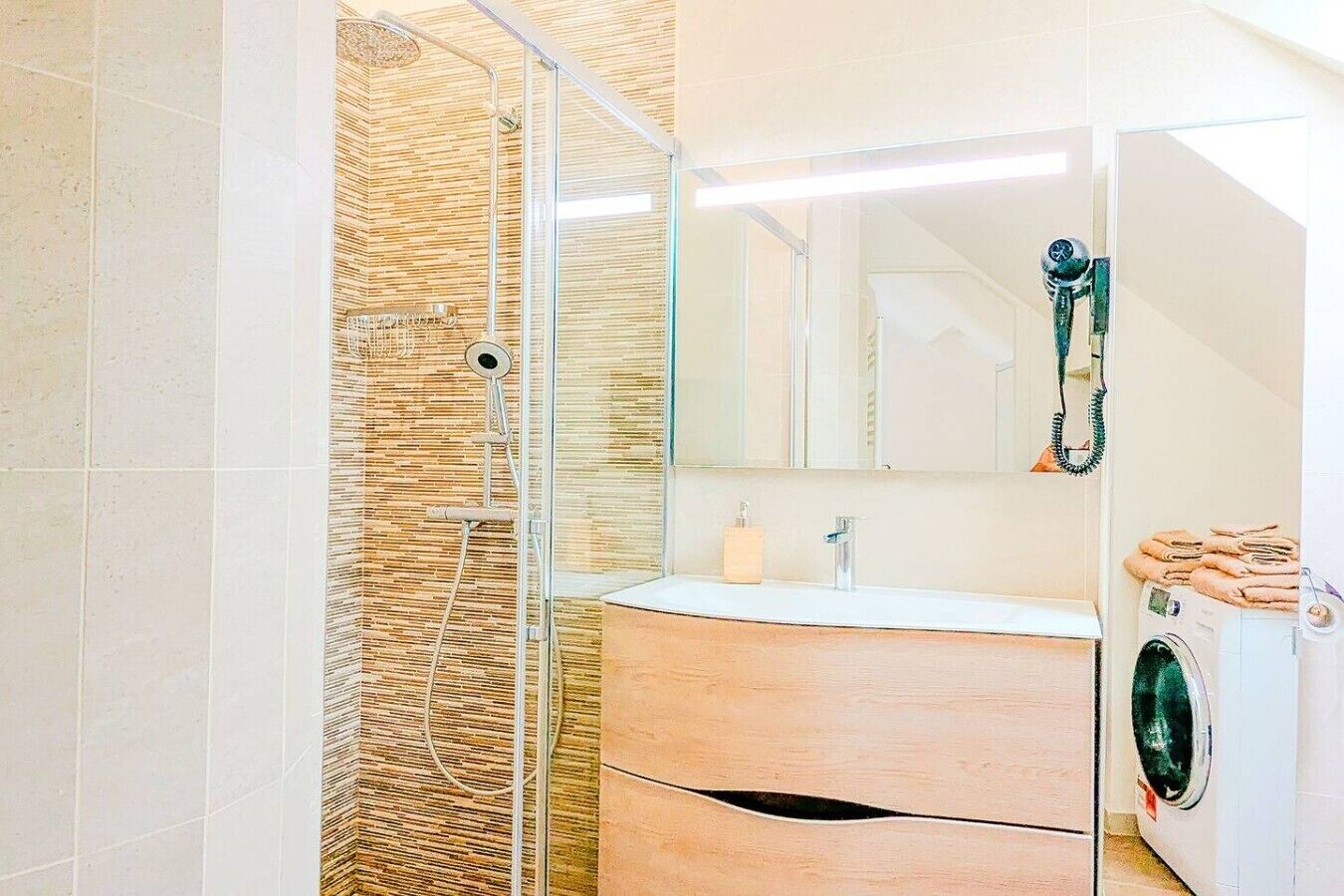 A bathroom with a shower, a sink, a mirror, and a washing machine.