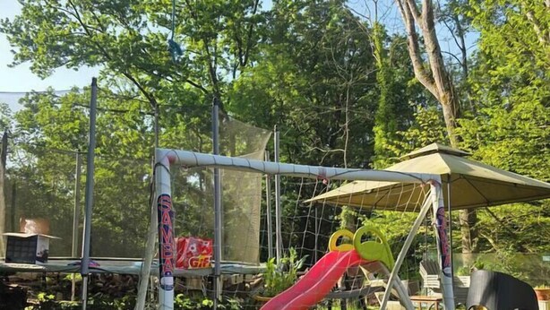 Uma área de lazer ao ar livre cercada, com um escorrega e gols de futebol com rede.