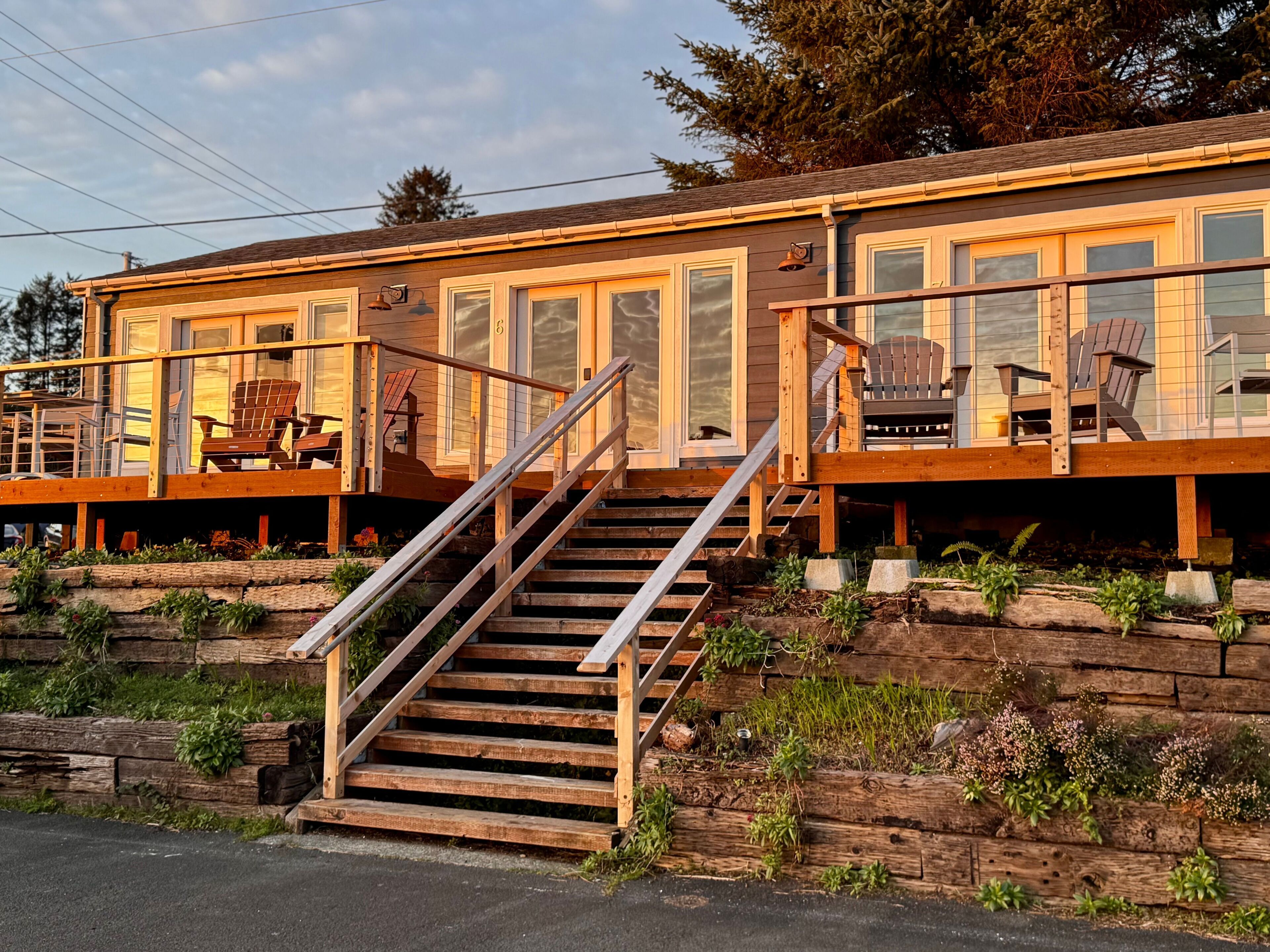 Un bâtiment en bois avec un escalier menant à une terrasse, comprenant un espace salon extérieur et offrant une vue sur le paysage environnant.
