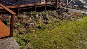 A wooden building labeled "Ocean Cove Inn" with a wooden deck and stairs leading up to it, surrounded by grass and a mountain in the background. - Ocean Cove Inn #8 - Ocean View (Yachats)