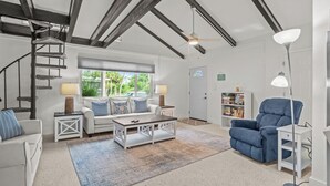 Een ruime woonkamer met een trap, een zithoek, een blauwe fauteuil en een boekenkast.